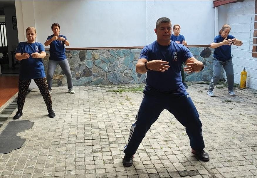 Clase de tai chi en el patio de XIHU: el instructor y cuatro alumnos en postura, Medellín